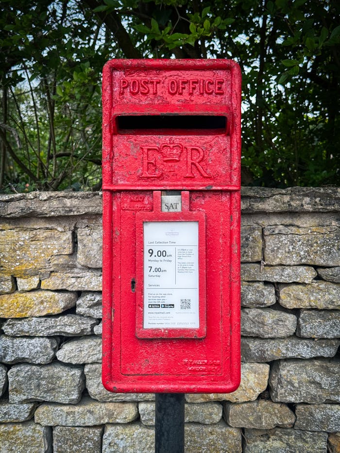 Classic red post box against a stone wall in Malmesbury, England, capturing a piece of British heritage.