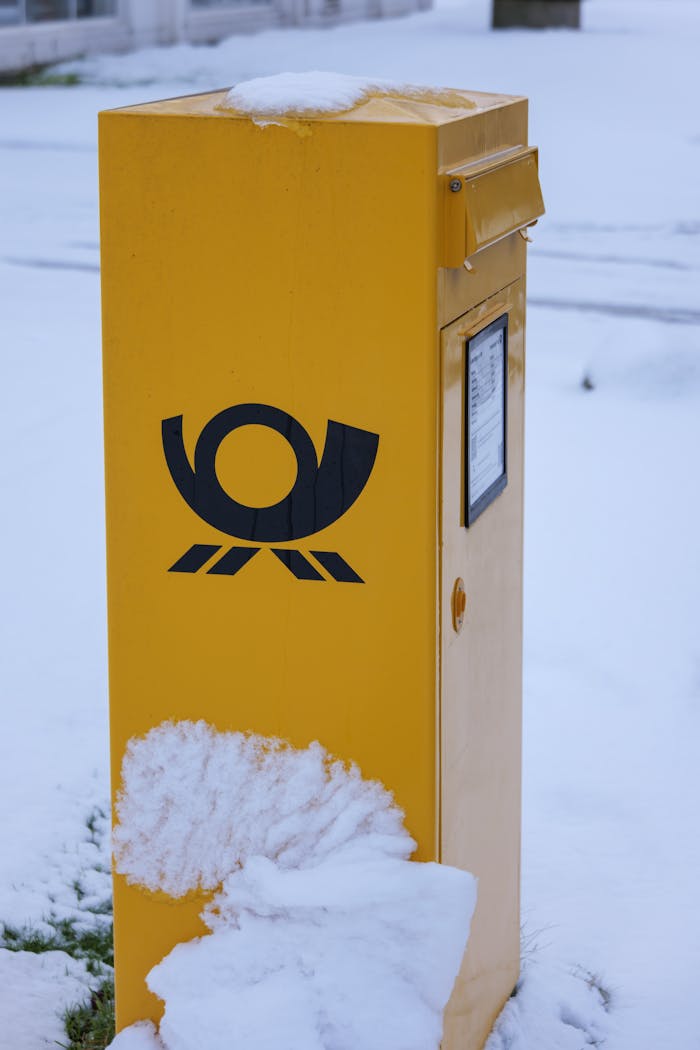 Bright yellow postal box covered in snow during winter, contrasting with the white surroundings.